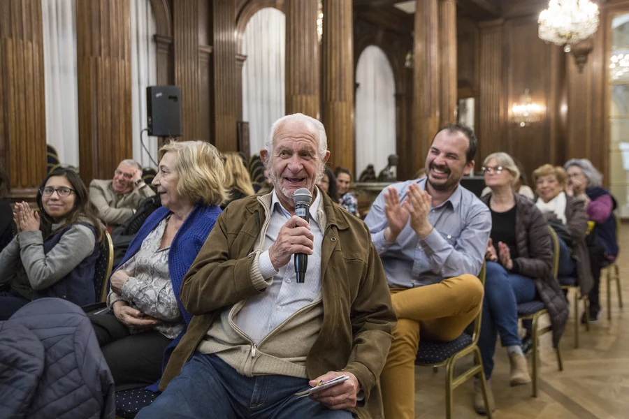 Un hombre mayor habla con micrófono ante un público que aplaude: voluntariado y participación sénior